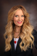 Woman with long blonde hair wearing a dark blazer and red heart necklace