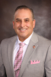Man with brown and gray hair wearing a light gray blazer and a striped long tie