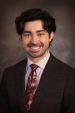 Man with black wavy hair wearing a business suit and neck tie