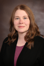 Amber Karpierz Woman with brown wavy hair wearing purple top and dark blazer
