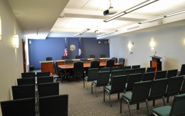 Photo of Commission room with chairs for the public, a podium for the public in front of a desk for elected officials