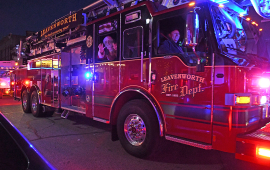 Santa and small child wave from the seat of a large fire truck lit up at night