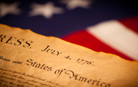 Photo of the front page of the Declaration of Independence with the words "congress" and "july 4 1776" in front of American flag