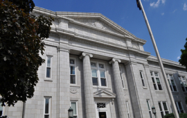 image of historic building with romanesque style columns, flagpole and red oak tree
