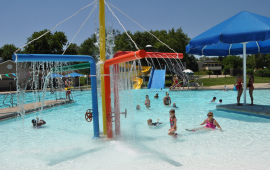 children play in a splash feature in a zero depth entry pool on a sunny day