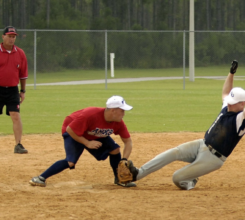 An adult male sliding into the base while another male is waiting at the base to tag him out on his foot