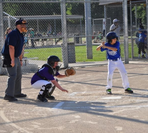 Umpire standing behind a young catcher waiting for a young batter to hit the ball