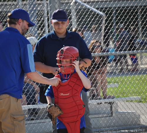 Picture of a coach talking to his young catcher during a baseball game with the umpire behind them