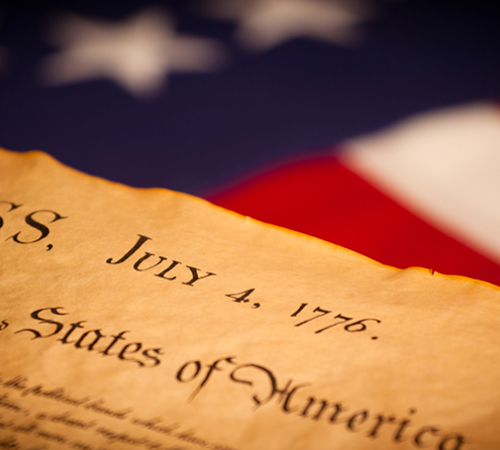 Photo of the front page of the Declaration of Independence with the words "congress" and "july 4 1776" in front of American flag