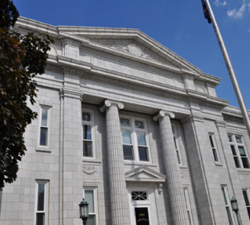 image of historic building with romanesque style columns, flagpole and red oak tree