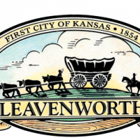 Logo of Leavenworth shows a covered wagon and set of cattle pointing left in in front of green grass and blue sky.
