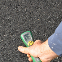 Digital readout of thermometer on recently paved asphalt shows 230.7 degrees Fahrenheit