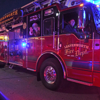 Santa and small child wave from the seat of a large fire truck lit up at night