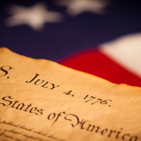Photo of the front page of the Declaration of Independence with the words "congress" and "july 4 1776" in front of American flag