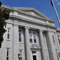 image of historic building with romanesque style columns, flagpole and red oak tree