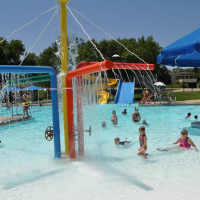 children play in a splash feature in a zero depth entry pool on a sunny day