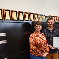 Finance team wins award Four people stand in front of filing cabinets with a line of award plaques on top. They are holding another award.