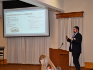 City Manager Scott Peterson Man dressed in suit and sport coat speaks at podium in front of a screen inside building