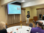 A speaker presents to people sitting at a table