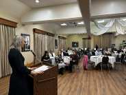 Brooke McCanles, Field Representative from U.S. Senator Roger Marshall's Office speaks at the Leavenworth Business Symposium Woman in black dress speaks to crowd seated at tables inside building