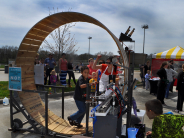 Child running in a giant hamster wheel while other children watch waiting for their turn at the game