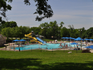 Wide shot of Wollman Aquatic Center showing grass, fence, slides, pool and shade structures