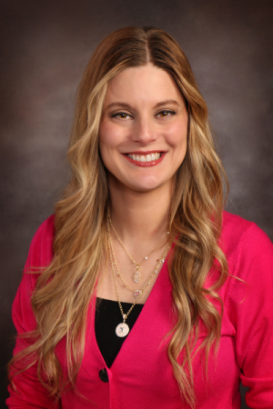 Woman with long blonde hair wearing a pink cardigan and necklace