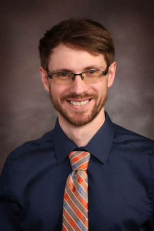 Man with brown hair and beard wearing glasses, button-down shirt and tie