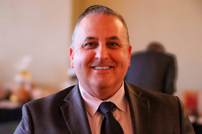 Photo of a man in a blazer with a white shirt and tie.