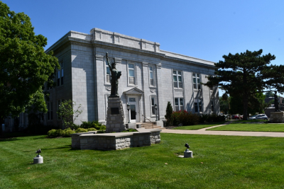 Photo of outside City hall, stone facade with green grass and trees, mini statue of liberty