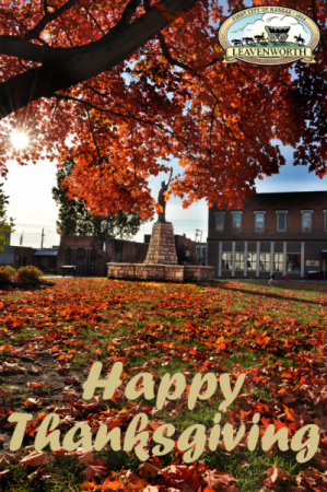 Tree with orange leaves, some on the ground, around mini Statue of Liberty, Leavenworth city logo text reads Happy Thanksgiving