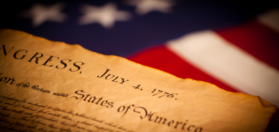 Photo of the front page of the Declaration of Independence with the words "congress" and "july 4 1776" in front of American flag