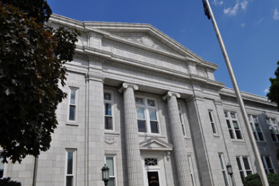 image of historic building with romanesque style columns, flagpole and red oak tree