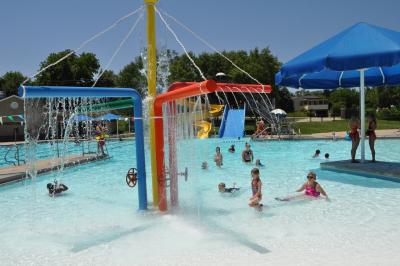 children play in a splash feature in a zero depth entry pool on a sunny day