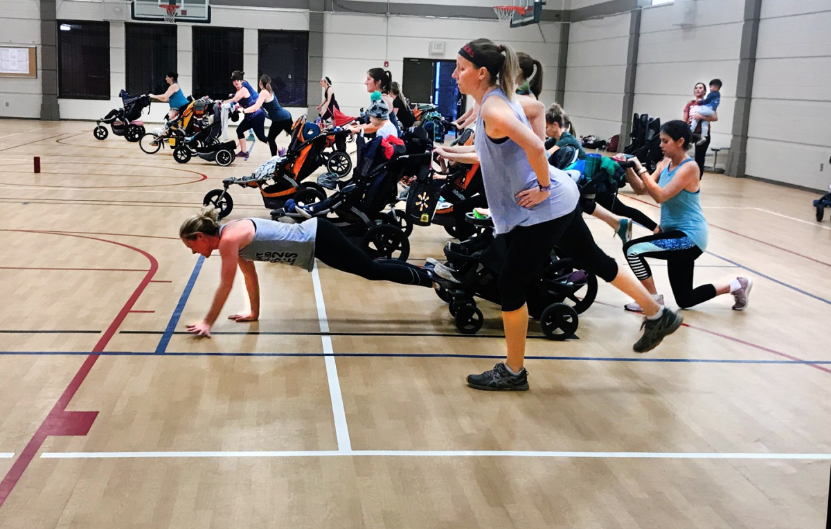 A group of moms running and walking with their strollers during the class in the Riverfront Community Center gym