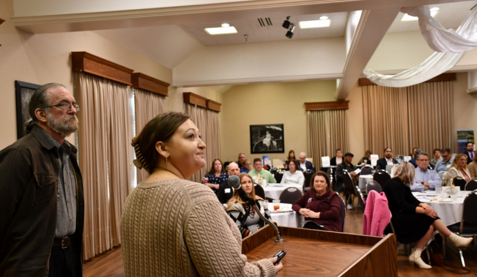 man and woman speak in front of podium to address audience seated at tables inside room