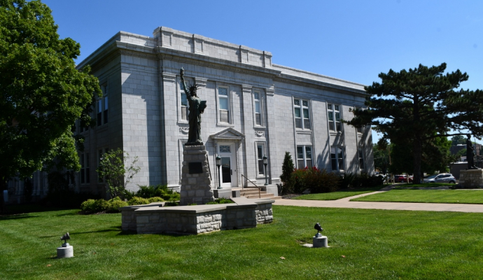 Photo of outside City hall, stone facade with green grass and trees, mini statue of liberty