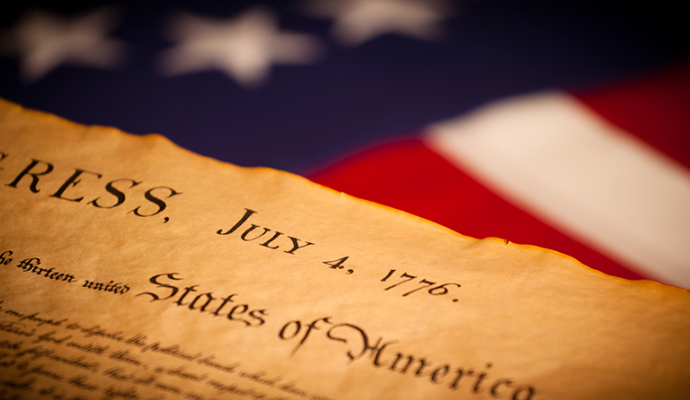 Photo of the front page of the Declaration of Independence with the words "congress" and "july 4 1776" in front of American flag