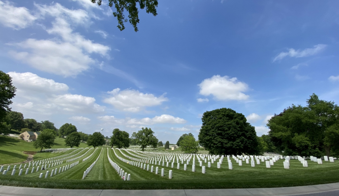 Photo of well kept cemetery in a green field with blue sky and trees